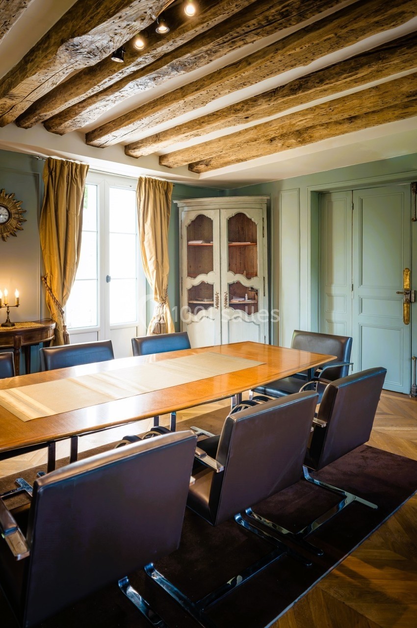 Salle à manger avec table en bois, chaises modernes, poutres apparentes au plafond et lumière naturelle.