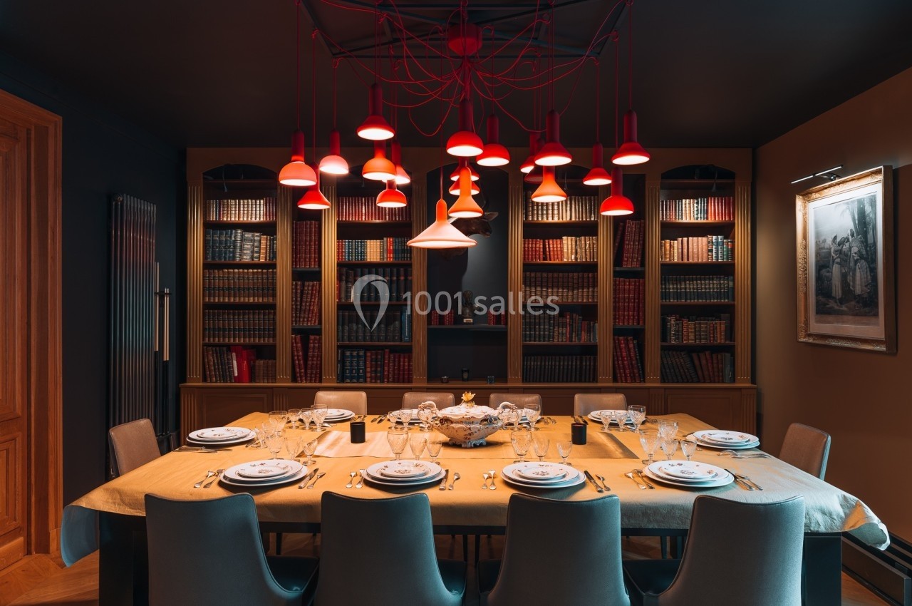 Salle à manger élégante avec une grande table dressée, entourée de chaises et éclairée par des suspensions rouges.