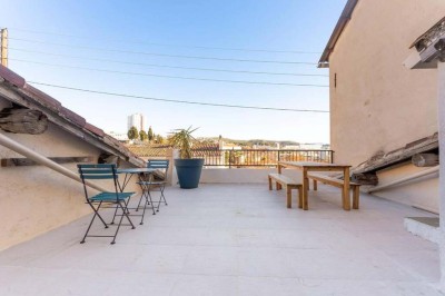 Chambre mansardée avec lit double, murs blancs et orange, sol en bois clair et tapis à motifs géométriques.