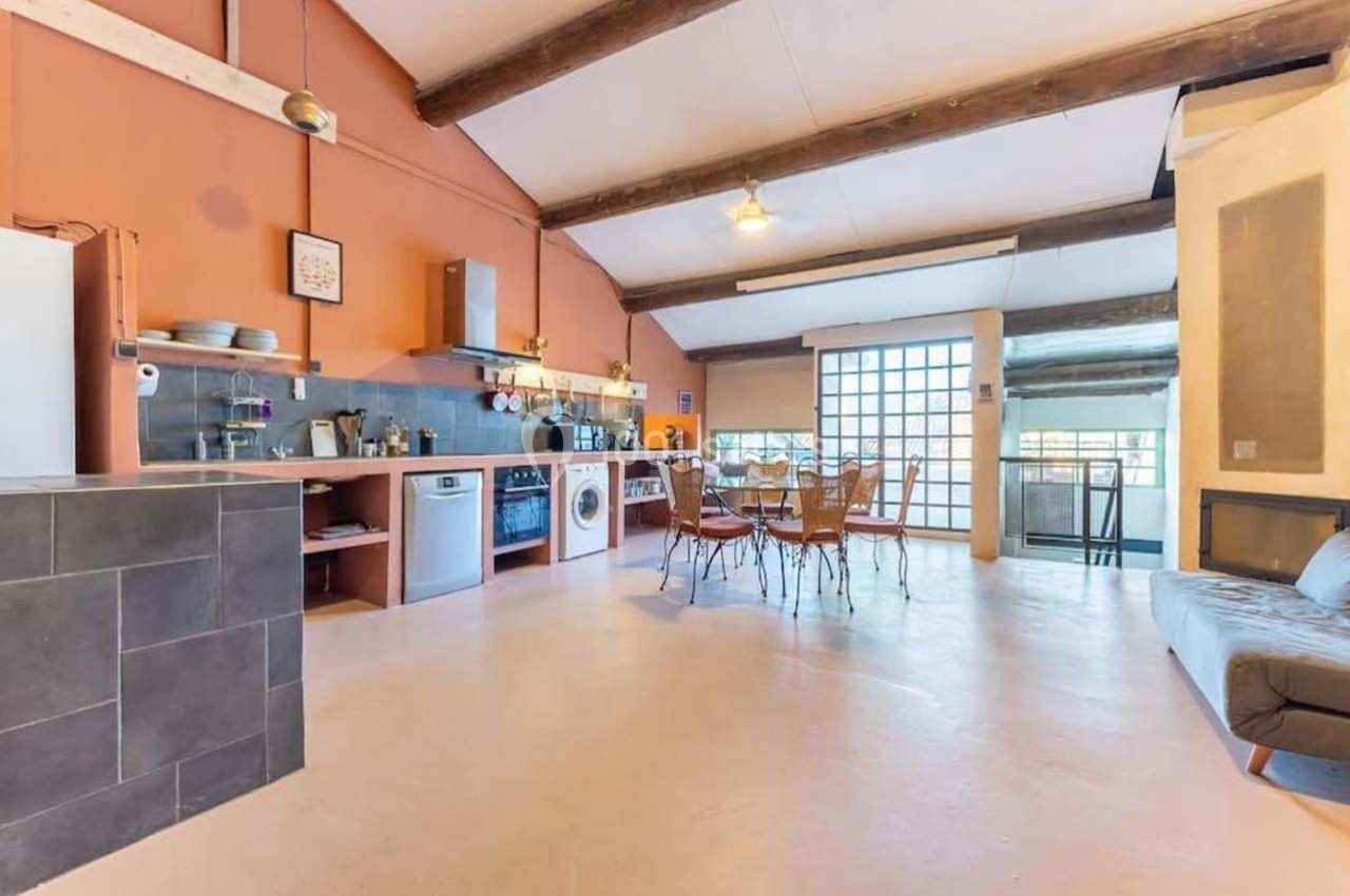 Cuisine ouverte avec murs orange, poutres apparentes, électroménagers modernes et coin repas avec table et chaises.