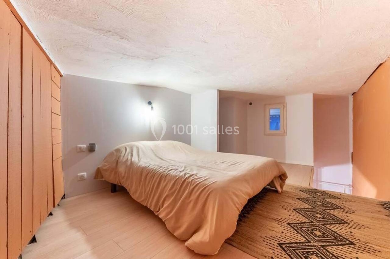 Chambre mansardée avec lit double, murs blancs et orange, sol en bois clair et tapis à motifs géométriques.