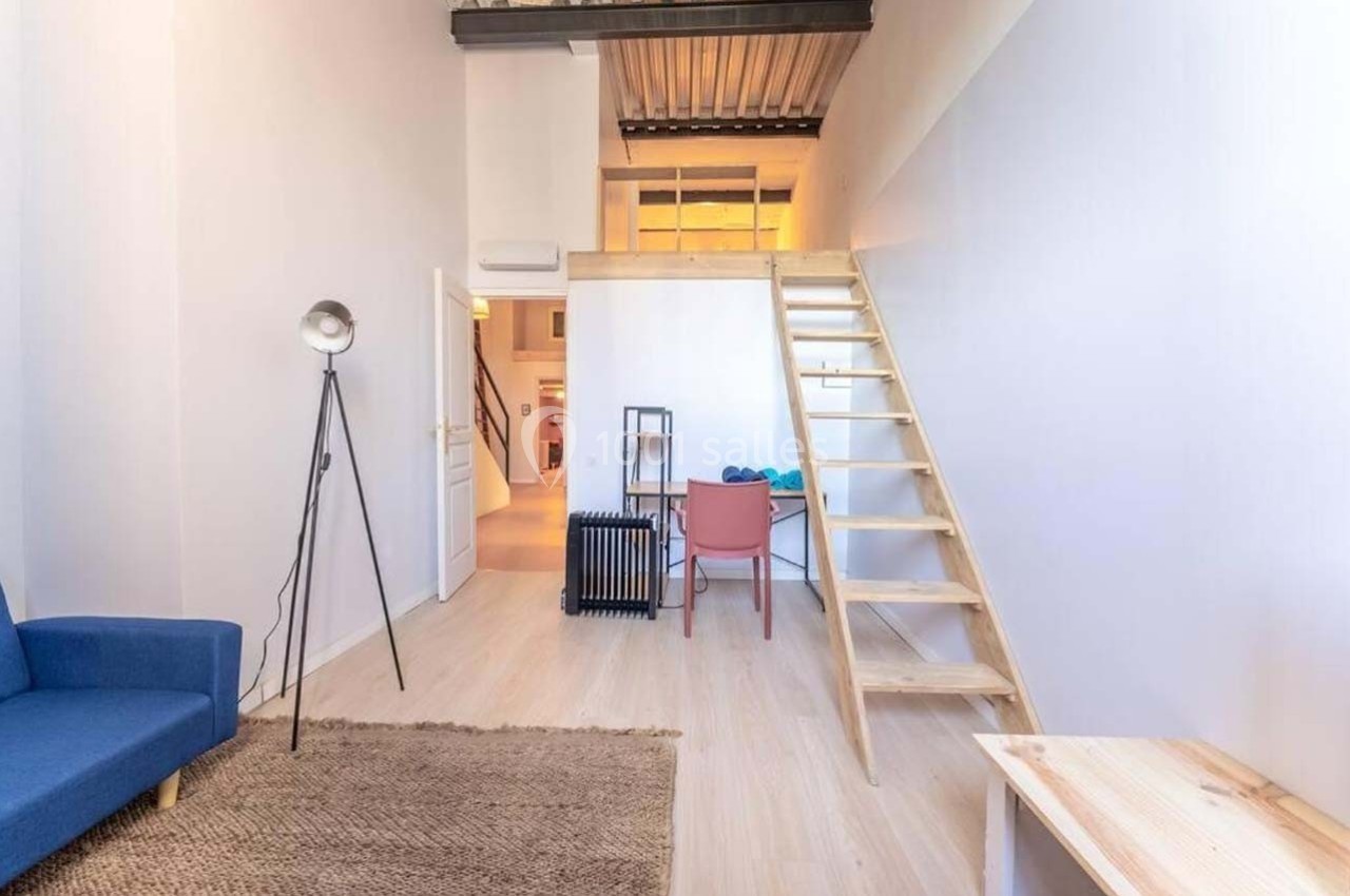Intérieur d'un studio lumineux avec mezzanine, échelle en bois, canapé bleu et mobilier minimaliste.