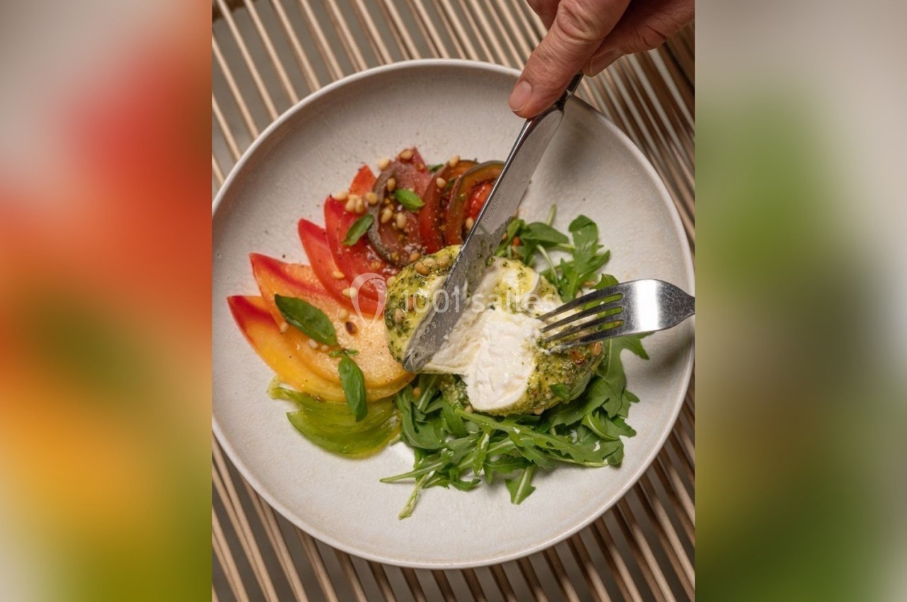 Assiette contenant une salade colorée avec tomates, roquette et fromage coupé à l'aide d'un couteau et d'une fourchette.