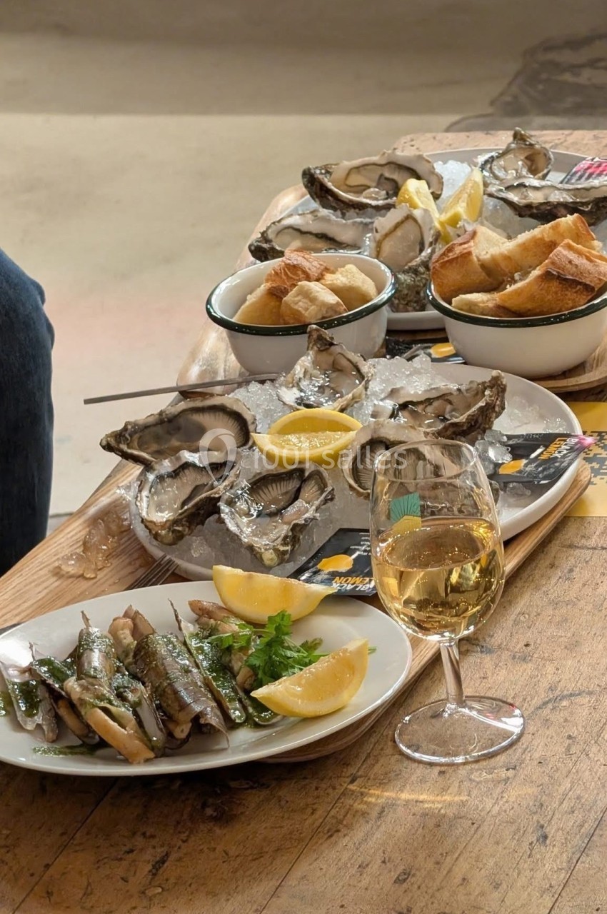 Plateau d'huîtres avec citron, sardines grillées, pain et verre de vin blanc sur une table en bois.