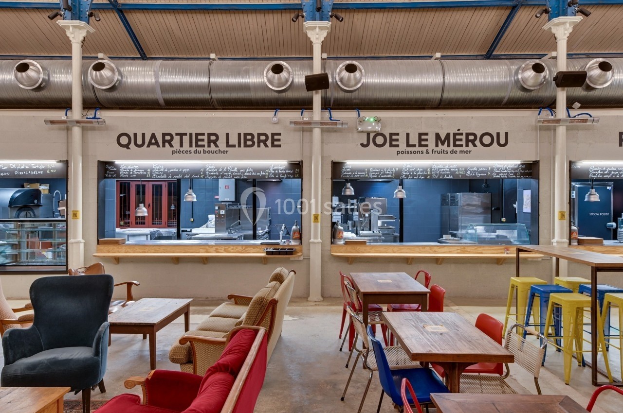 Intérieur d'un espace de restauration avec comptoirs, tables, chaises colorées et décoration industrielle.