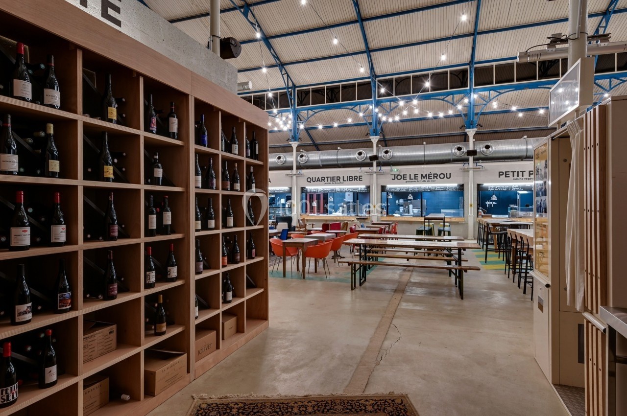 Rayonnages de bouteilles de vin dans un espace intérieur lumineux avec tables et stands de restauration en arrière-plan.