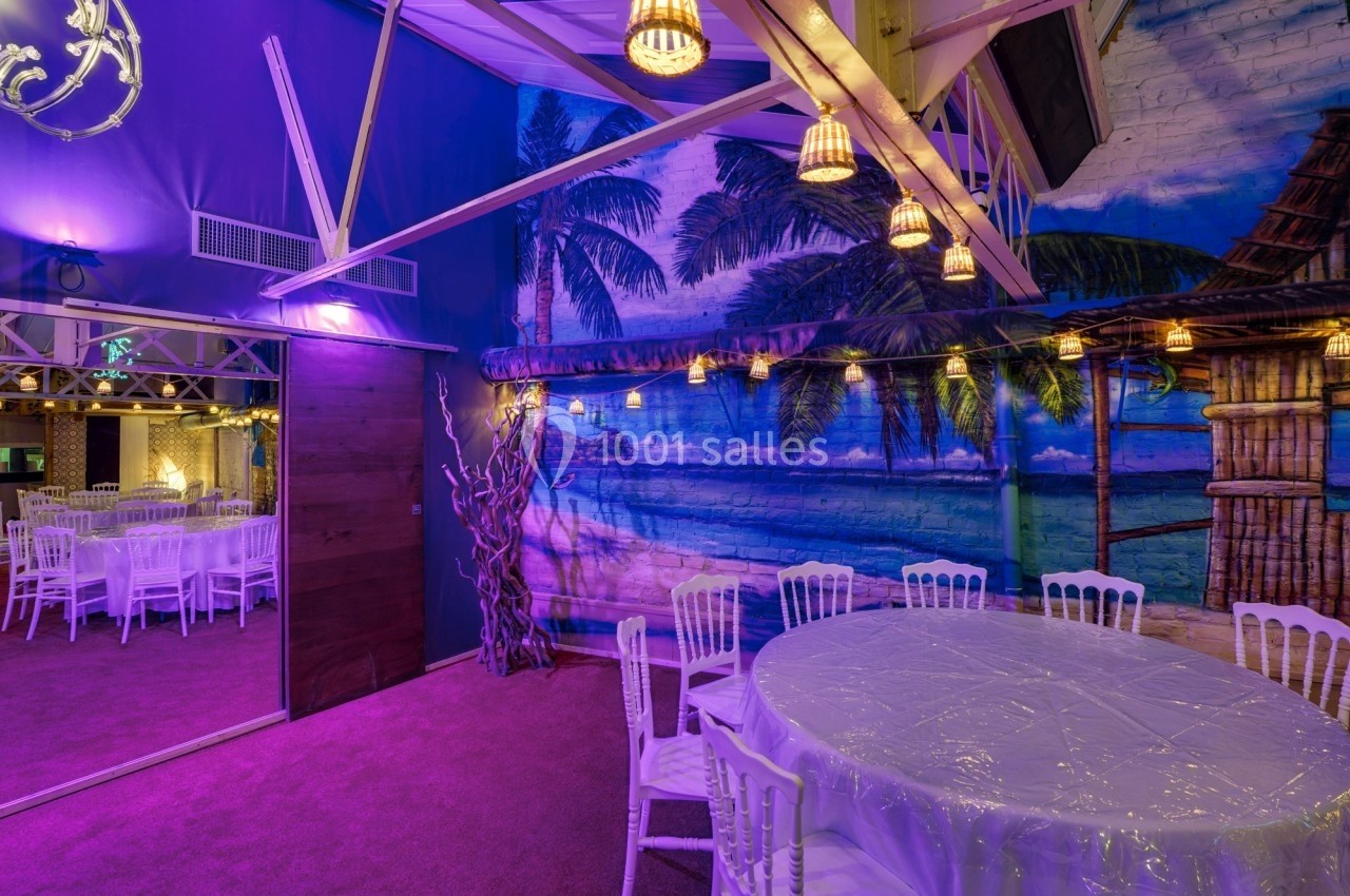 Salle décorée avec fresque tropicale, tables rondes recouvertes de nappes blanches et éclairage violet tamisé.