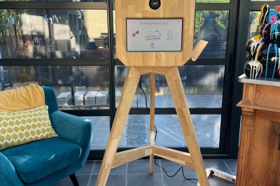 Borne photo en bois sur trépied, équipée d'un écran et d'un objectif, installée dans un jardin avec des coquelicots au…