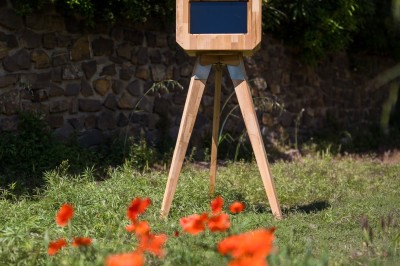Miniature M-Photobooth #4 Borne photo en bois sur trépied, équipée d'un écran et d'un objectif, installée dans un jardin avec des coquelicots au…