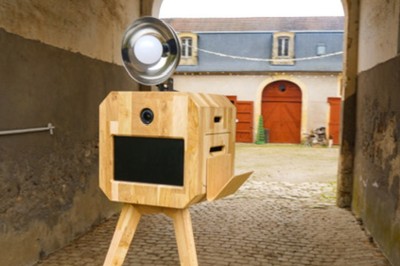 Miniature M-Photobooth #3 Borne photo en bois sur trépied, équipée d'un écran et d'un objectif, installée dans un jardin avec des coquelicots au…