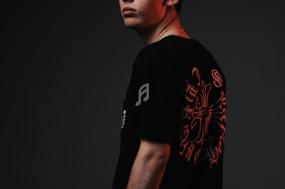 Un homme debout, vêtu d'un t-shirt noir avec un motif rouge dans le dos, regarde par-dessus son épaule.