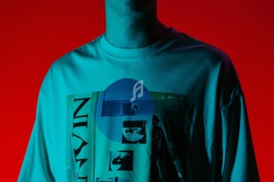 Jeune homme debout, éclairé par une lumière rouge et bleue, portant un t-shirt imprimé graphique.