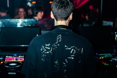 Un DJ de dos mixant dans une boîte de nuit sombre, éclairée par des lumières rouges et des boules à facettes.