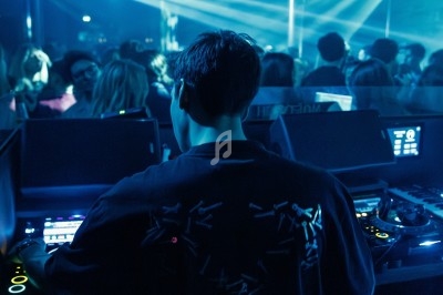 Un DJ mixe dans une boîte de nuit sombre, éclairée par des lumières bleues et des boules à facettes.