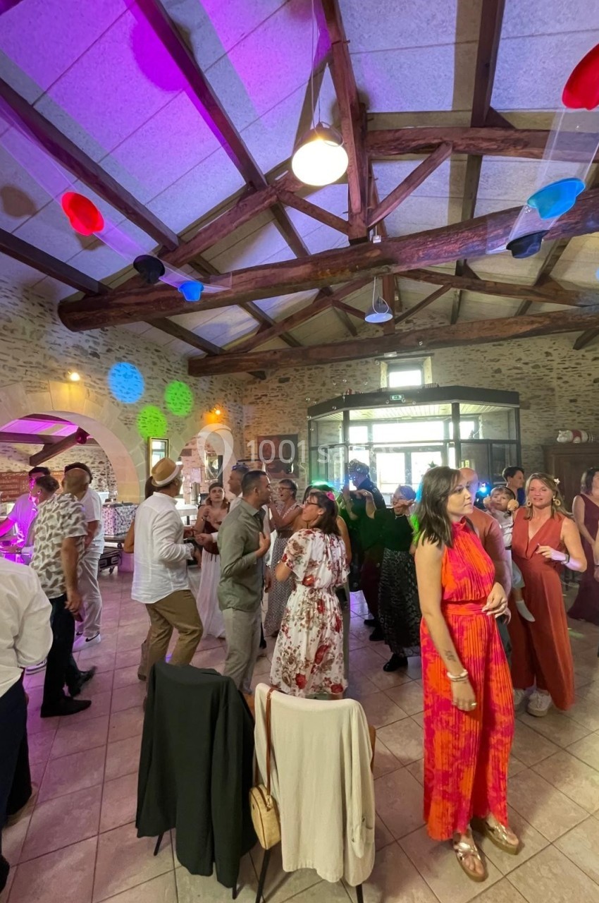 Des personnes dansent et discutent dans une salle en pierre avec des lumières colorées et un plafond en poutres apparentes.