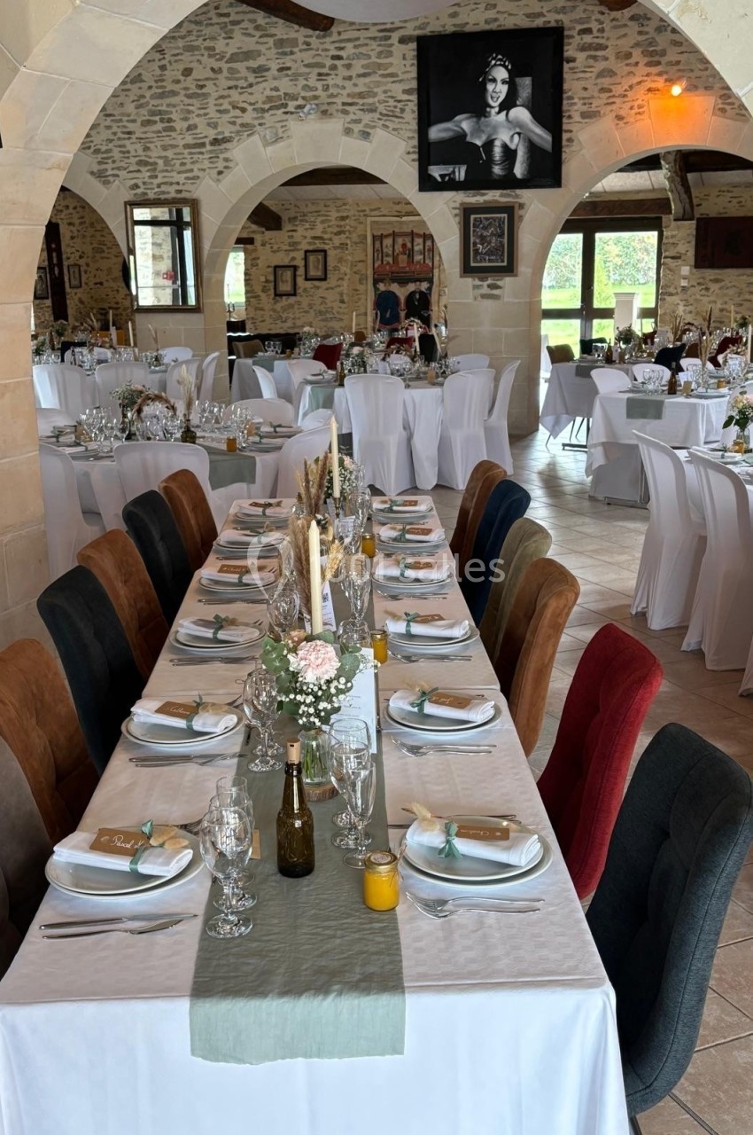 Salle de réception décorée pour un événement, avec tables dressées, chaises colorées et murs en pierre apparente.