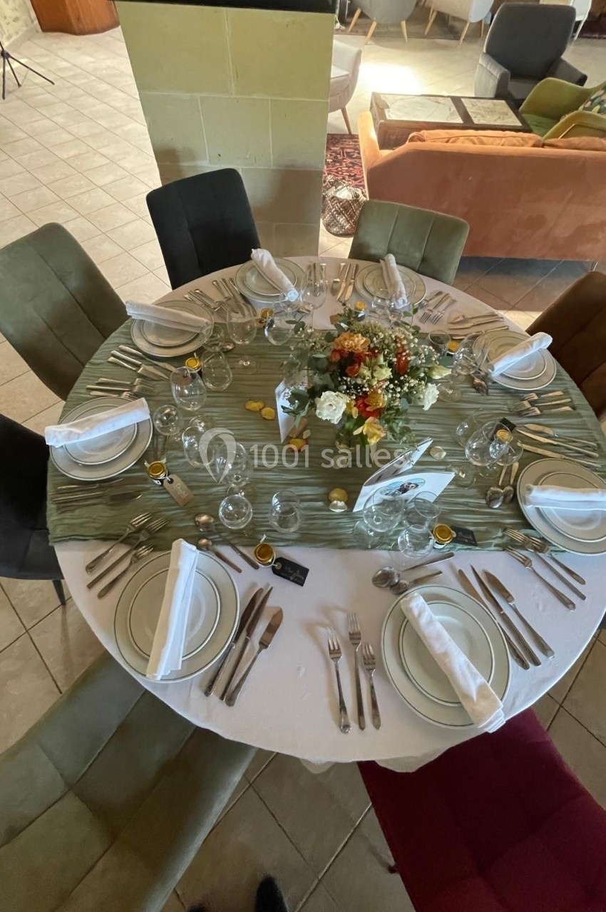 Table ronde élégamment dressée avec nappes, couverts, serviettes pliées, verres et un centre de table floral.