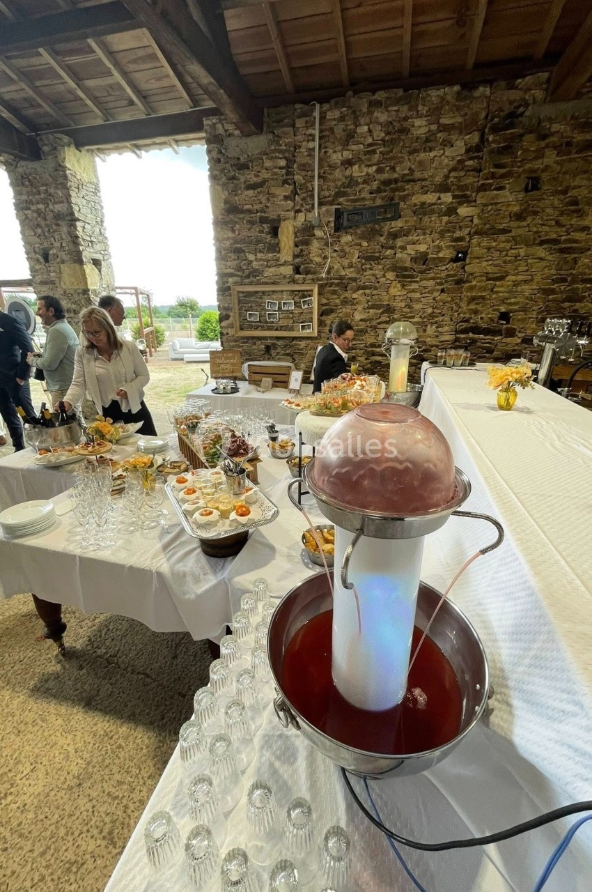 Buffet de réception avec fontaine à boisson, plats variés et décor rustique sous une charpente en bois.