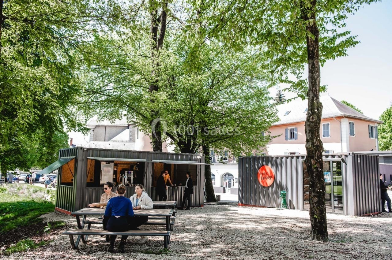 Des personnes discutent à une table de pique-nique près de conteneurs aménagés, entourés d'arbres et de bâtiments.