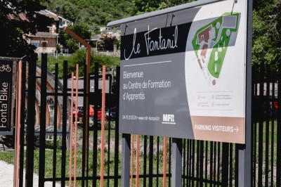 Façade d'un bâtiment commercial avec enseigne ’Comera Cuisines’ et affiches publicitaires, entouré de végétation.