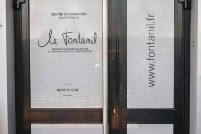 Façade d'un bâtiment commercial avec enseigne ’Comera Cuisines’ et affiches publicitaires, entouré de végétation.
