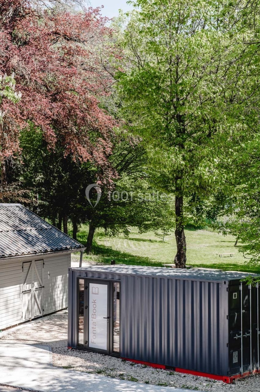 Un conteneur noir aménagé en espace fonctionnel, placé près d'un bâtiment clair dans un cadre arboré.
