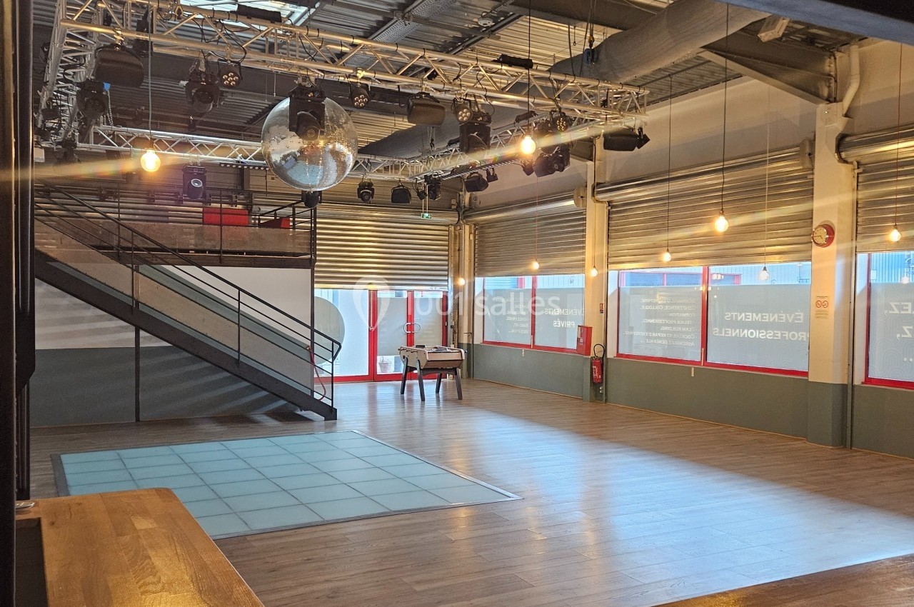 Salle polyvalente avec parquet, piste de danse, mezzanine, éclairage suspendu et grande baie vitrée.