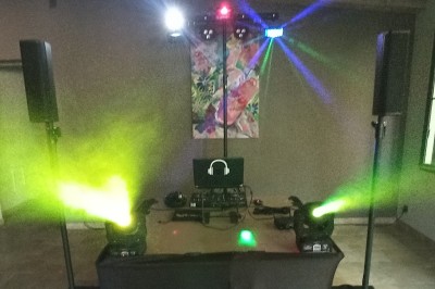 Un DJ en chemise rouge se tient derrière une table de mixage avec des lumières colorées en arrière-plan.