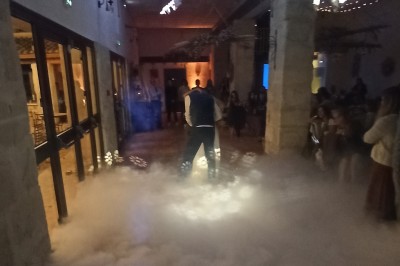 Un DJ en chemise rouge se tient derrière une table de mixage avec des lumières colorées en arrière-plan.