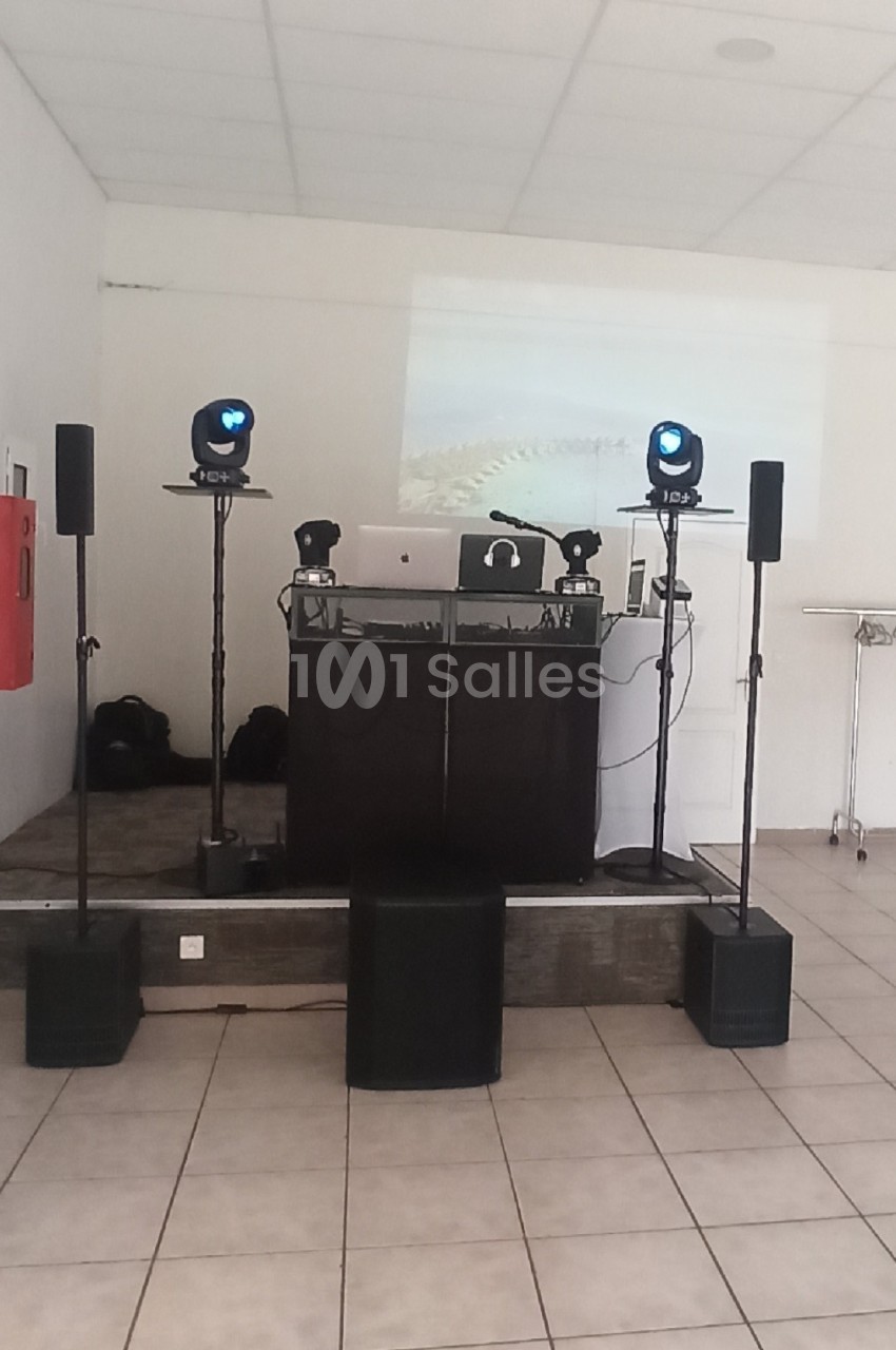 Cabine DJ équipée d'une console, ordinateur, casque et projecteur sur podium surélevé - aménagement pour animation événementielle en salle.