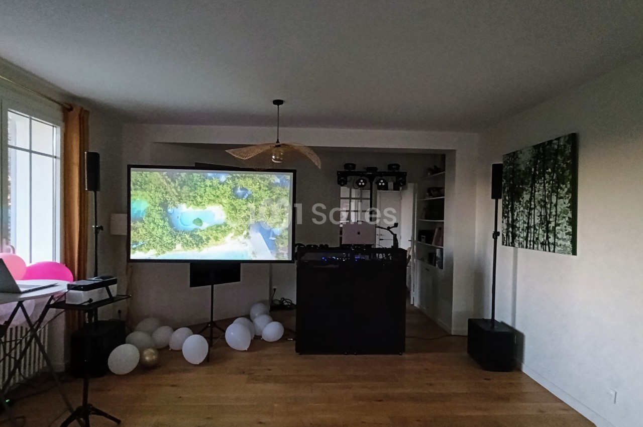 Salle intérieur avec écran de projection, console DJ noire et ballons blancs au sol.