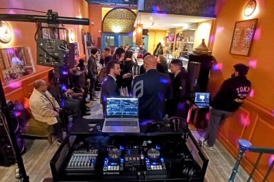 Vue d'une soirée dans un bar avec des invités discutant et une table de mixage en premier plan.