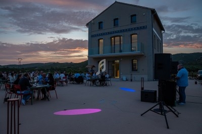 Groupe de personnes dînant en plein air au coucher du soleil devant un bâtiment moderne avec éclairages colorés.