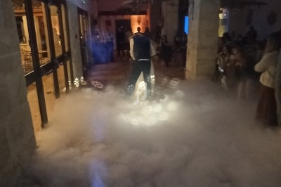 Un couple danse au milieu d'une piste entourée de fumée dans une salle éclairée par des lumières tamisées.