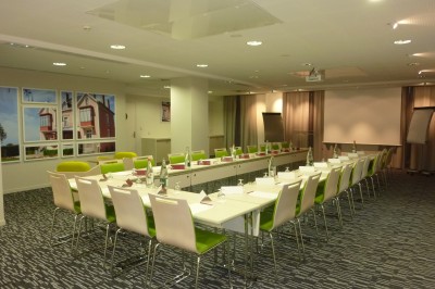 Salle de réunion lumineuse avec tables disposées en U, chaises vertes et blanches, et matériel de présentation.