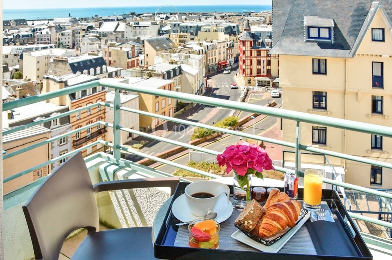 Petit-déjeuner avec viennoiseries, café et jus d'orange sur une terrasse surplombant une ville côtière.