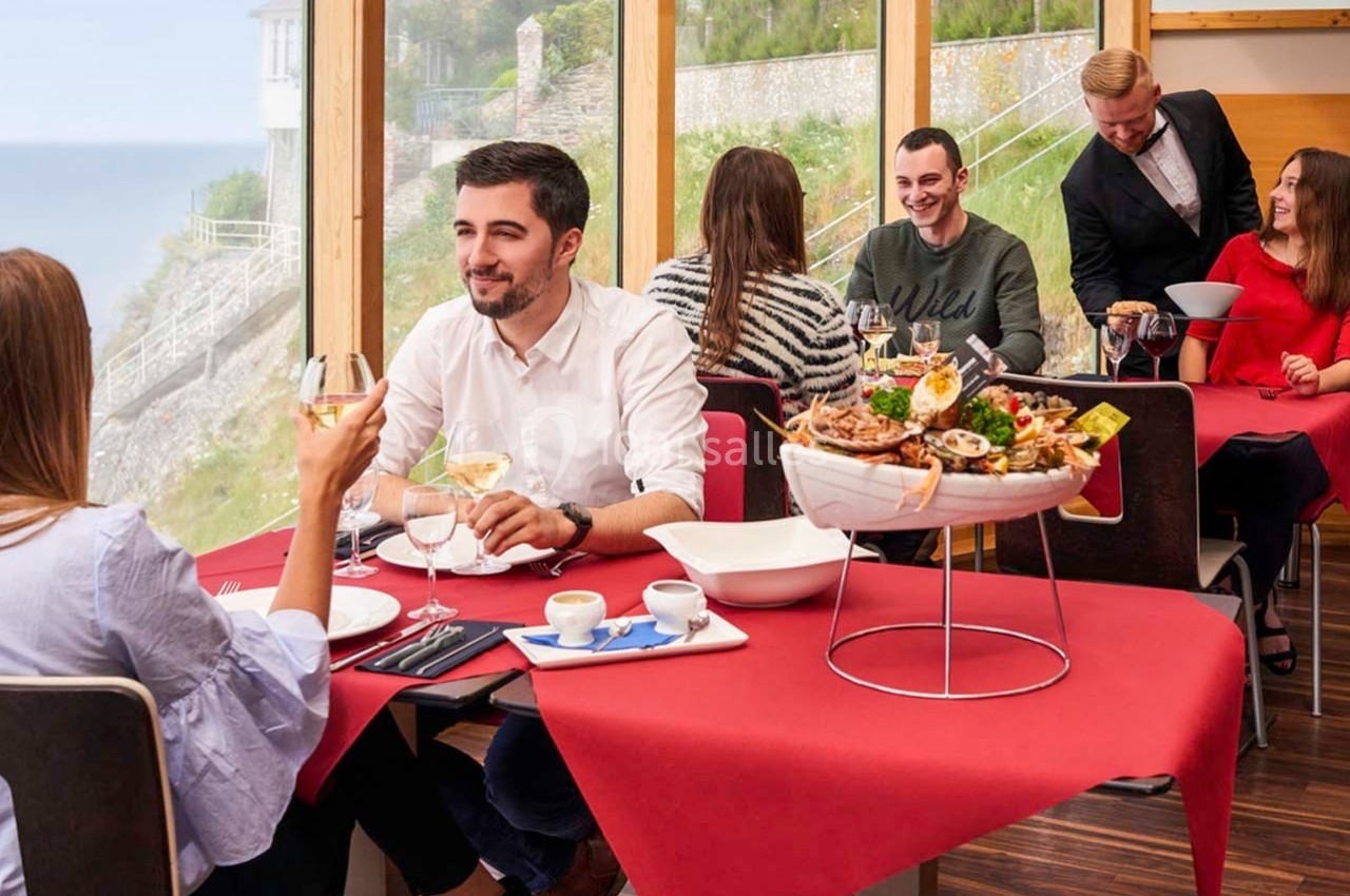Des personnes dînent dans un restaurant avec vue sur la mer, dégustant des fruits de mer et du vin blanc.