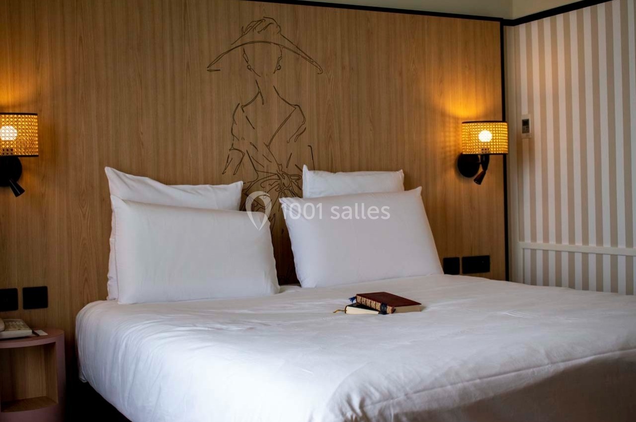 Lit double avec draps blancs, encadré par deux appliques murales allumées, dans une chambre au décor minimaliste.