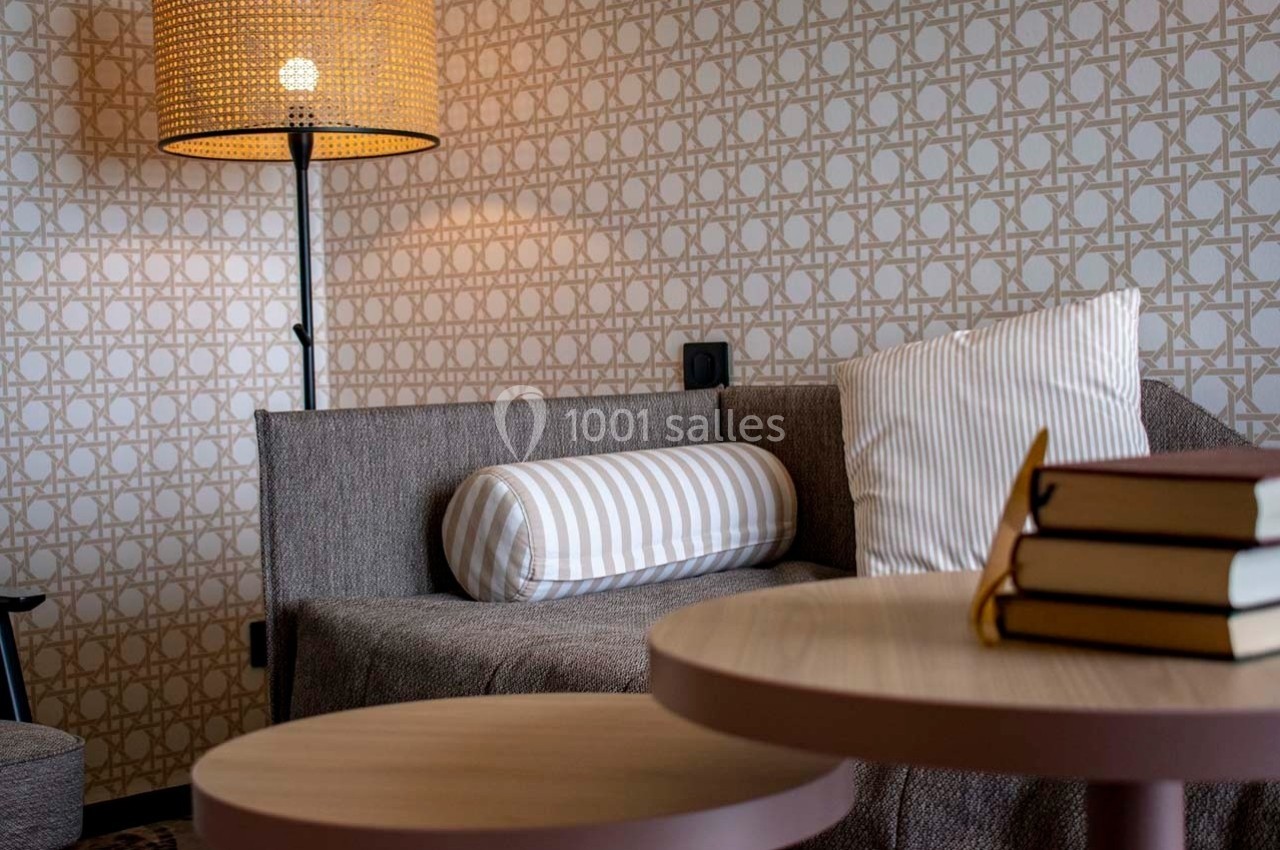 Canapé gris avec coussins rayés, lampadaire en rotin allumé et tables basses en bois, dans un intérieur cosy.