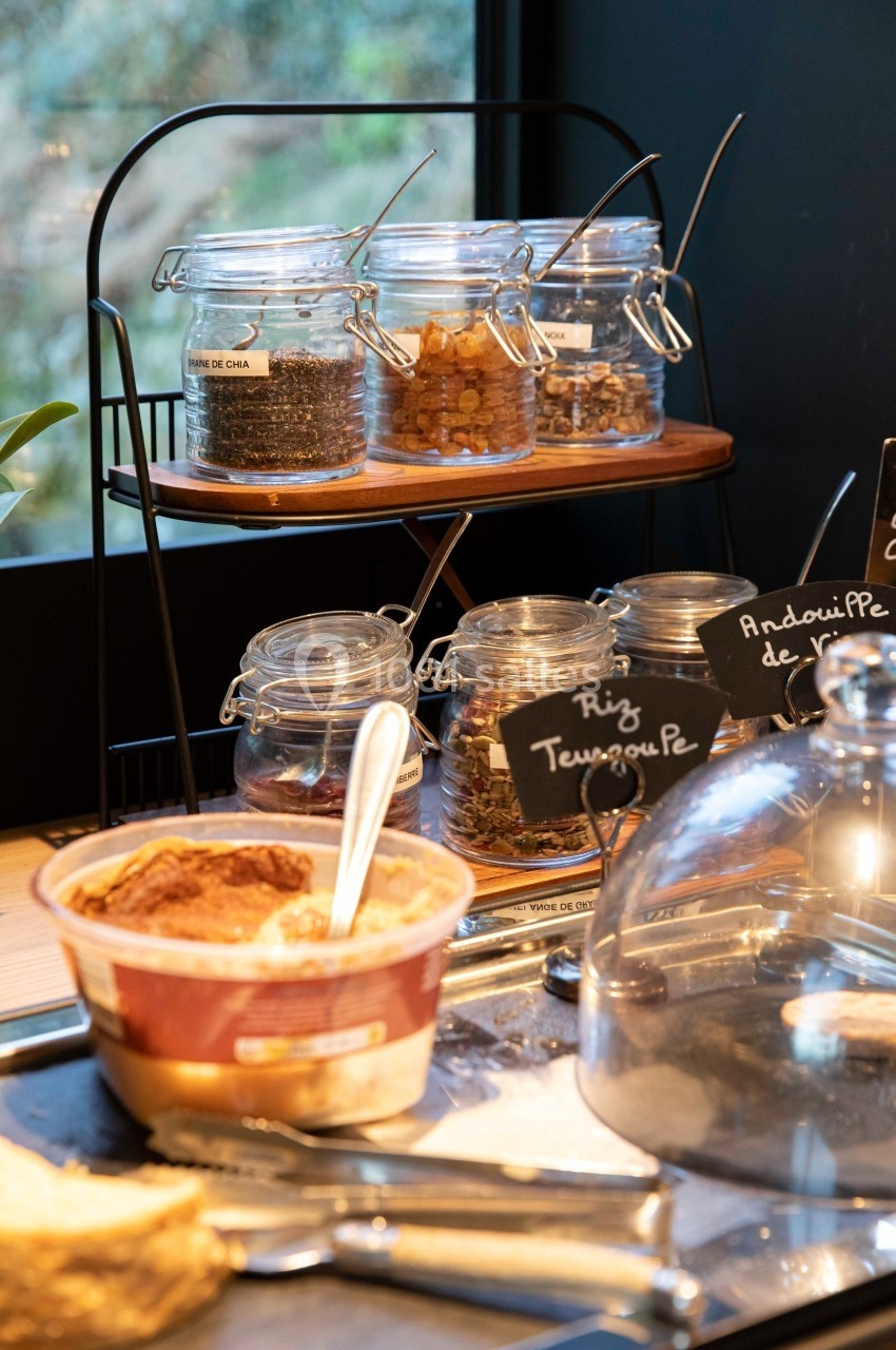 Bocaux de graines et céréales sur une étagère, avec un bol de nourriture et des étiquettes en ardoise au premier plan.