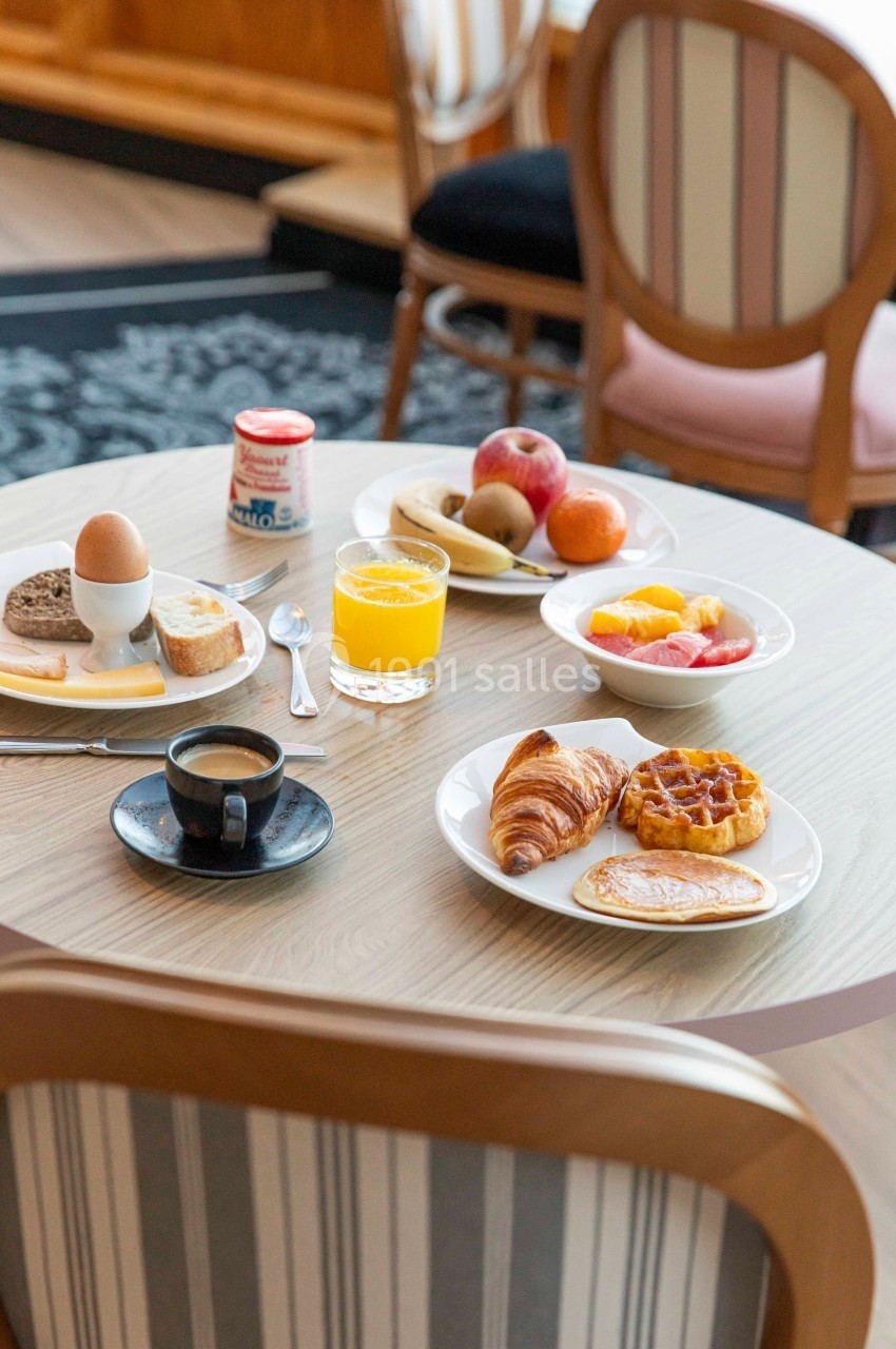 Petit-déjeuner servi sur une table avec croissant, gaufre, fruits, œuf à la coque, café et jus d'orange.