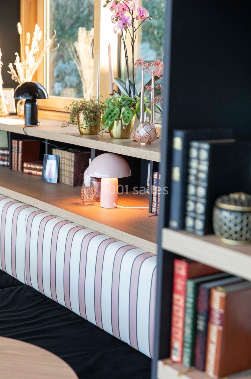 Étagère en bois avec livres, plantes, bougies et objets décoratifs, éclairée par une lumière naturelle.