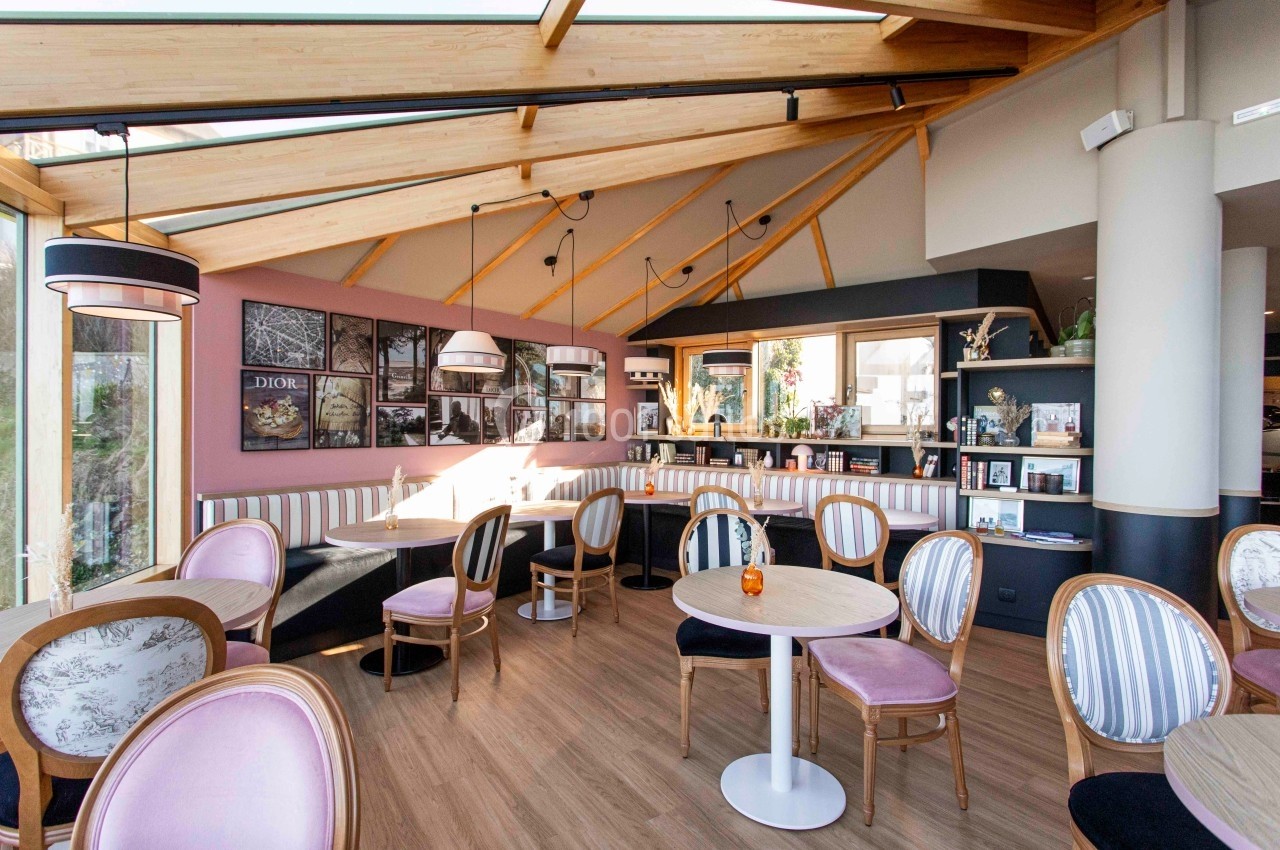 Salle lumineuse d’un café moderne avec des tables rondes, des chaises élégantes et une décoration murale artistique.