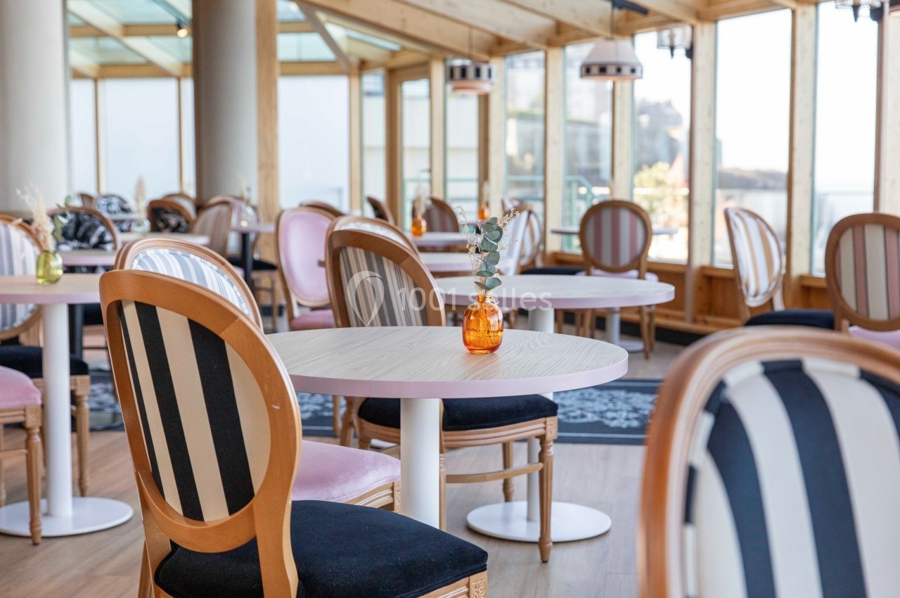 Salle lumineuse avec des tables rondes, des chaises rayées et des vases décoratifs dans un cadre moderne en bois.