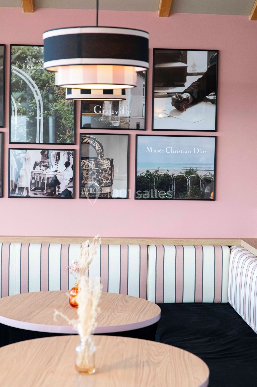 Banquette rayée et tables en bois clair dans un café décoré de cadres photos sur un mur rose.