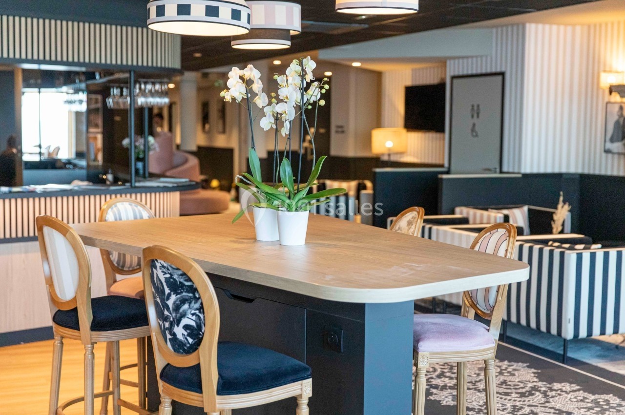 Salle moderne avec table haute en bois, chaises élégantes, orchidées en pot et décoration intérieure raffinée.