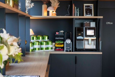 Bureau en bois clair avec une chaise, une machine à café, des tasses et une lampe murale allumée dans une chambre.