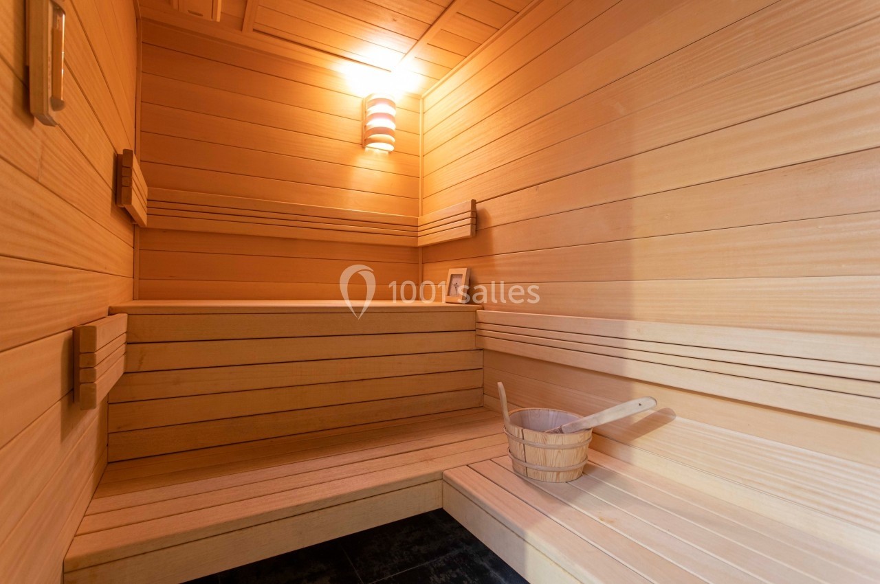Intérieur d'un sauna en bois clair avec bancs, seau en bois et lumière douce au mur.