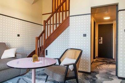 Bureau en bois clair avec une chaise, une machine à café, des tasses et une lampe murale allumée dans une chambre.