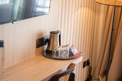 Bureau en bois clair avec une chaise, une machine à café, des tasses et une lampe murale allumée dans une chambre.